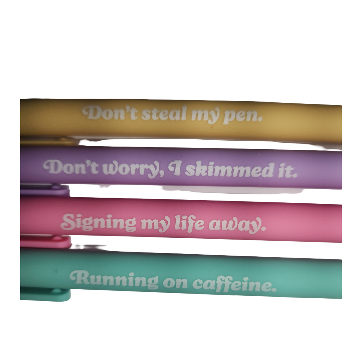 Close-up of four pastel message pens in yellow, purple, pink and teal, showing their playful printed sayings.